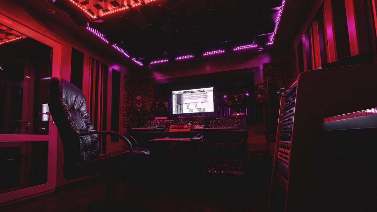 Régie de studio : fauteuil, console, écran et enceintes sous un éclairage rouge et violet